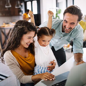 Junge Familie im Homeoffice: Eltern arbeiten am Computer, während ihr Kind zwischen ihnen sitzt.