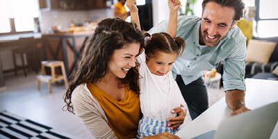 Junge Familie im Homeoffice: Eltern arbeiten am Computer, während ihr Kind zwischen ihnen sitzt.